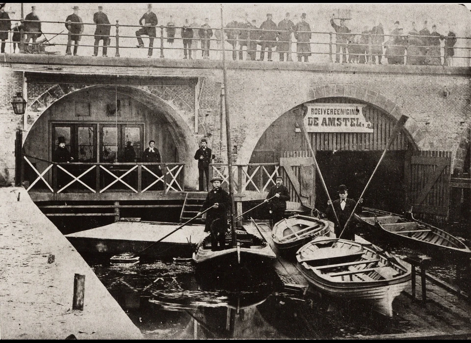 De club en botenloods van Roeivereniging De Amstel onder de bogen van de Hogesluis (1877)